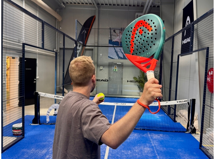 Man håller upp en grön och röd HEAD Radical padelracket med en padelboll – test för spelare på mellannivå